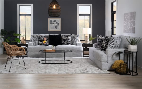 Transitional Glacier White 93'' sofa and chair set with plush white polyester fabric, Bob-O-Pedic memory foam cushions, six patterned accent pillows, black metal oval coffee table, and woven chair in modern living room.