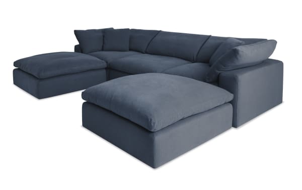 Dream Navy 131'' 5 Piece Modular Sectional in navy blue fabric with 2 corners, 2 ottomans, and 1 armless chair. Transitional style with reversible, oversized cushions in polyester and nylon blend upholstery. Part of the Dream collection, featuring modular design for customizable living room seating.