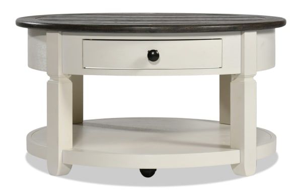 Round farmhouse-style Laurel Entertainment & Occasional coffee table in white MDF with a distressed brown top, storage drawer, and lower shelf.