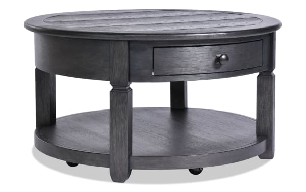 Round charcoal farmhouse coffee table from Laurel Entertainment & Occasional collection, made of MDF with a distressed top, storage drawer, and lower shelf.