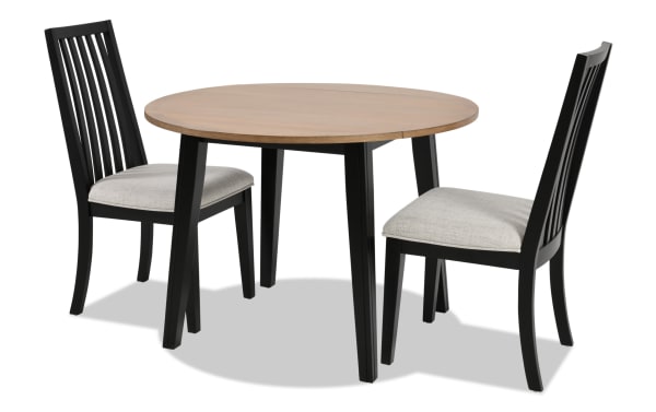 Blake 3 Piece Black & Natural Upholstered Dining Set with two gray fabric polyester cushioned slat-back chairs and round drop-leaf table in MDF and hardwood solids, featuring a transitional cottage-style design ideal for small kitchens and apartments.