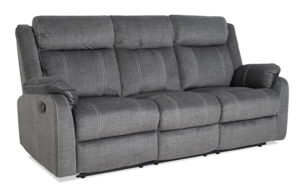Lagoon Gray 81'' manual reclining sofa in transitional style, upholstered in soft gray polyester fabric with plush padded cushions and visible white stitching.