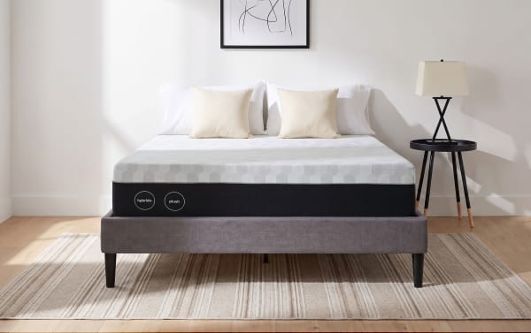 12" Hybrid Queen Plush Mattress with plush comfort and tight-top tailoring on a gray upholstered bed frame, shown with neutral pillows and adjustable base compatible design.