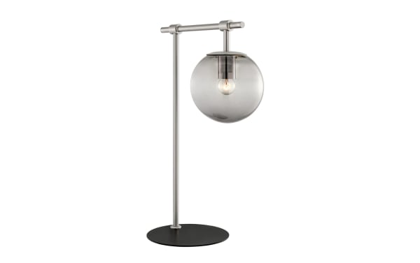 Ezra Nickel Table Lamp with transitional style, nickel frame, black base, and clear glass globe shade showcasing an ambient bulb for warm lighting.
