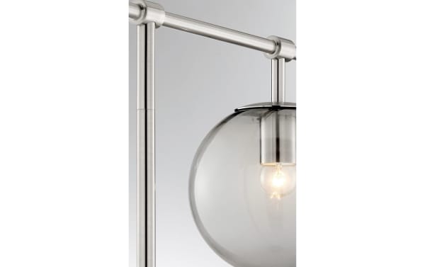 Ezra Nickel Table Lamp with transitional style, featuring a clear glass globe shade and brushed nickel frame, showcasing an exposed ambient bulb.
