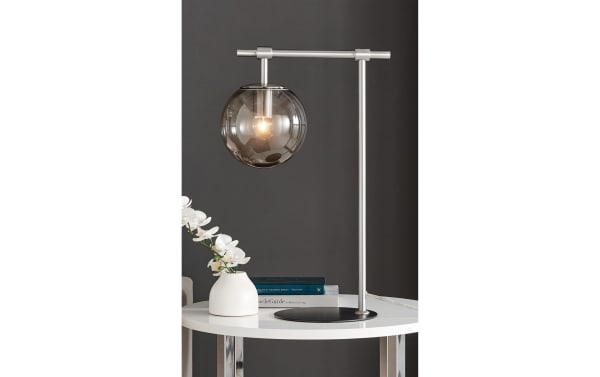 Ezra Nickel Table Lamp with transitional style, nickel frame, and smoky glass globe shade, offering warm ambient lighting for modern interiors.