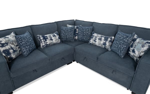 Dark blue fabric sectional sofa with corner design, featuring multiple patterned throw pillows in blue, white, and gray tones, ideal for modern living rooms.