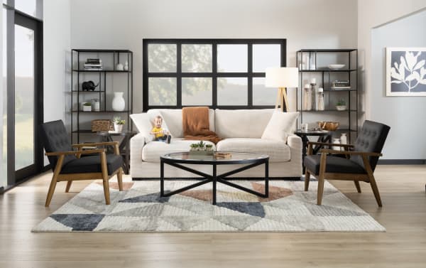 Beige Aspen 78'' transitional sleeper sofa with plush polyester fabric upholstery, cushy accent pillows, and a black metal round coffee table on a patterned rug.