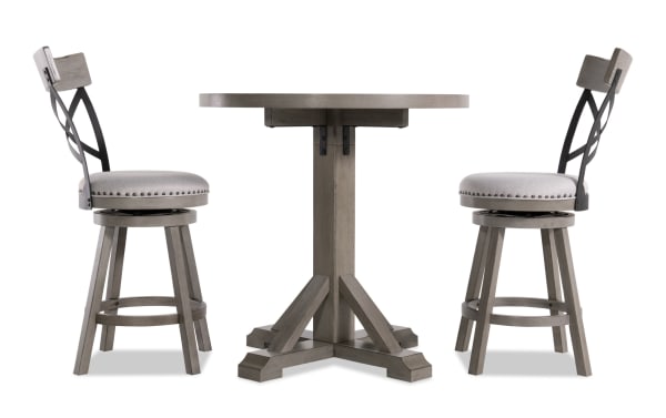 Gray Iris 3 Piece Upholstered Adjustable Height Round Dining Set with swivel stools, nailhead trim, cross-back design, and pedestal table base.