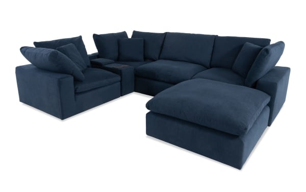 Dream Navy 131'' 6-piece modular sectional in navy blue polyester fabric with 3 corners, armless chair, console with USB/USB-C ports, and ottoman. Transitional style with oversized reversible cushions and feather blend toppers.