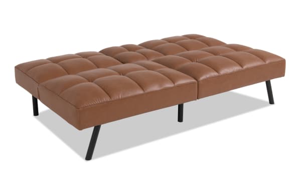 Dallas Cognac Futon in transitional style with brown faux leather upholstery, tufted seat cushions, and black angled legs, ideal for versatile living spaces.