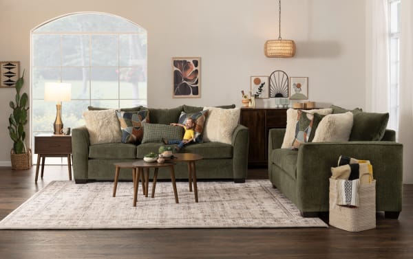 Transitional Brynn collection living room with green polyester fabric sofas, plush pillows, wooden tables, and decorative storage basket.