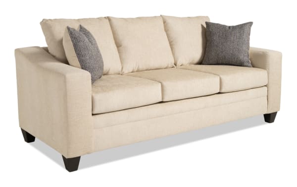 Claudia 84'' beige transitional sofa upholstered in soft polyester fabric, featuring three seat cushions, three back cushions, and two gray accent pillows for added comfort.