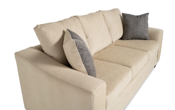 Claudia 84'' beige sofa in transitional style with soft polyester fabric upholstery, featuring three seat cushions and two gray accent pillows for comfort.
