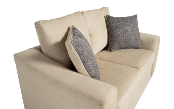 Claudia 62'' beige loveseat in transitional style with soft polyester fabric upholstery, featuring two textured gray accent pillows for added comfort.