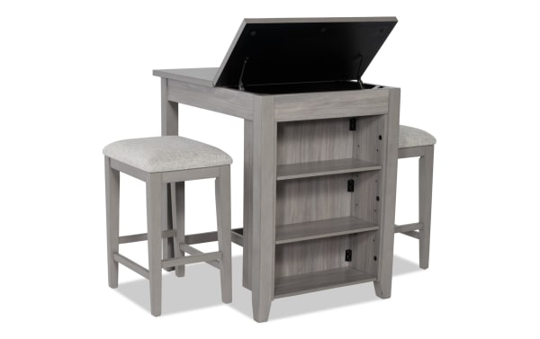 Homeworks 3 Piece Gray Upholstered Counter Height Kitchen Island Set with lift-top storage, adjustable shelves, and cushioned polyester stools in transitional style.