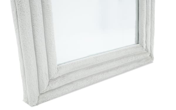 Close-up of a corner of a soft, plush light gray fabric frame around a mirror, highlighting the textured, padded design and stitching details.