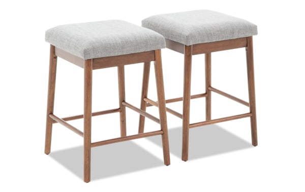 Two wooden bar stools with light gray upholstered seats, mid-century modern style, featuring tapered legs and horizontal footrests.