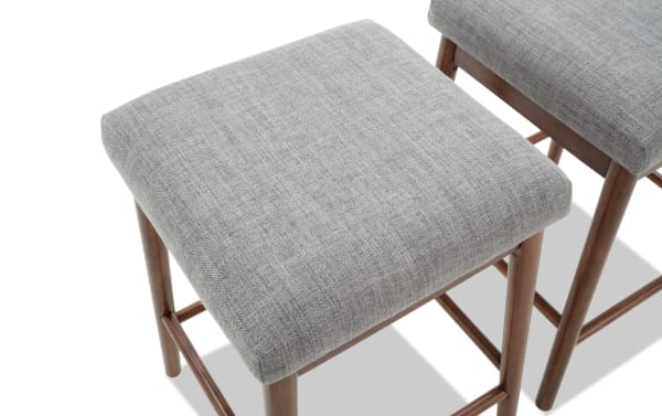 Square gray fabric upholstered stool with wooden legs and crossbars, modern minimalist design for home or office seating.