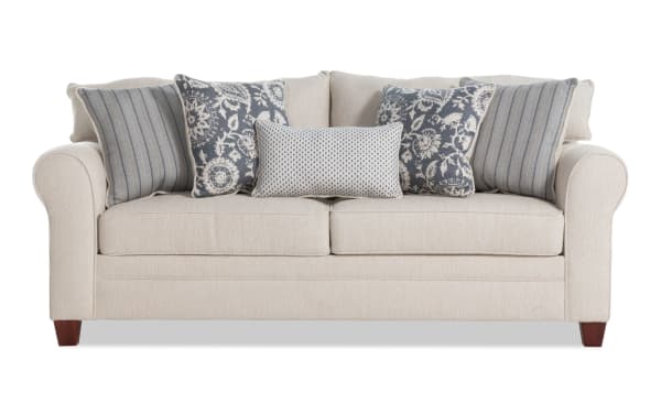 Beige Portland 85'' transitional sleeper sofa with soft polyester fabric upholstery, rolled arms, and five patterned accent pillows for added comfort.