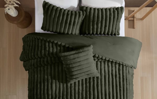 Dark green plush velvet bedding set on a bed, featuring ribbed texture pillows and comforter for a cozy, modern bedroom look.