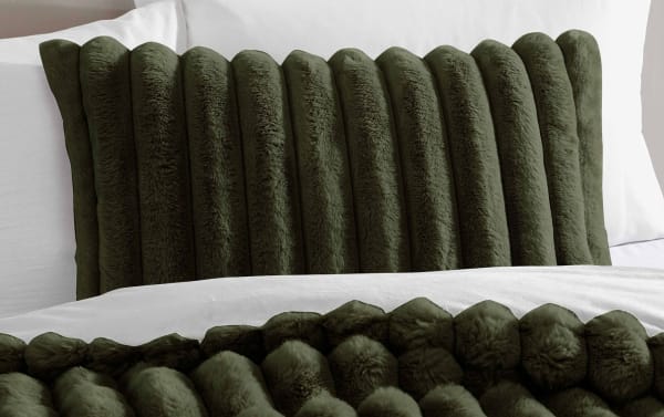 Dark green faux fur lumbar pillow with vertical channel tufting on a white bed with matching dark green faux fur blanket, showcasing cozy bedroom decor.
