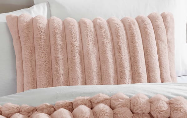 Soft, plush pink faux fur lumbar pillow with vertical ribbed texture on a white bed, enhancing bedroom decor and comfort.