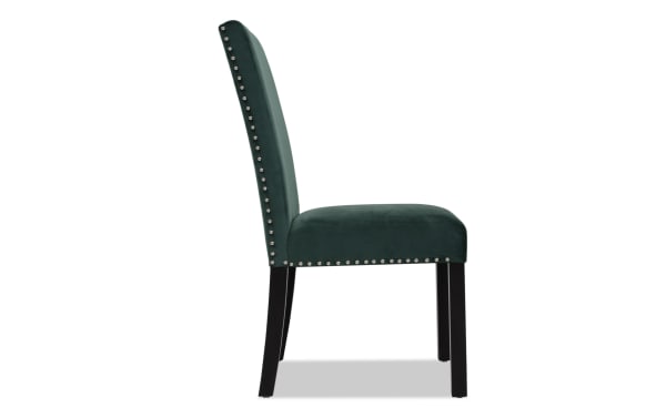 Upholstered dining chair with dark green velvet fabric, high backrest, silver nailhead trim, and black wooden legs, side view.