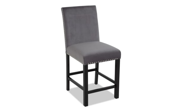 Gray upholstered counter-height chair with black wooden legs, silver nailhead trim, and padded backrest, suitable for kitchen or bar seating.