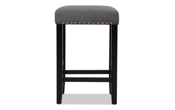 Gray upholstered bar stool with silver nailhead trim, black wooden legs, and footrest, suitable for kitchen or bar seating.