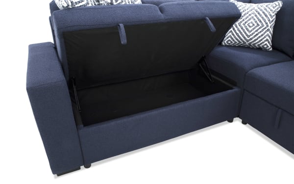 Blue fabric sectional sofa with storage compartment under the seat, featuring black interior lining and patterned throw pillows.