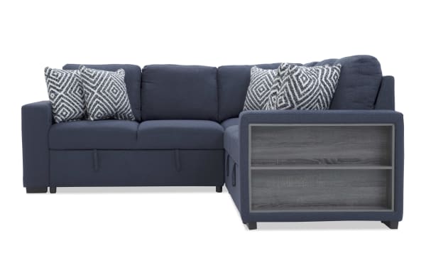 Navy blue fabric sectional sofa with corner design, built-in side shelves in wood finish, and five patterned gray and white throw pillows.