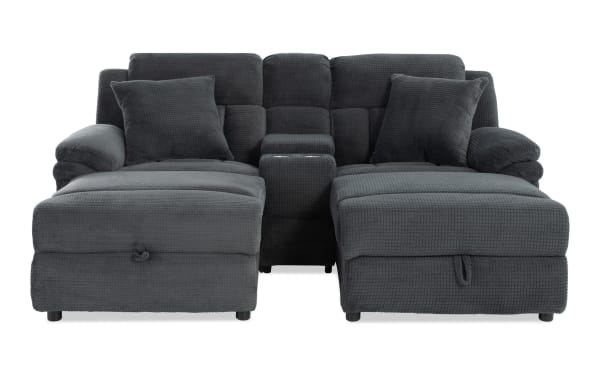 Dark gray fabric reclining sectional sofa with two chaise lounges, padded armrests, two matching throw pillows, and a central console with cup holders.