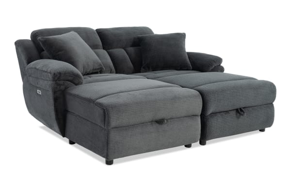 Dark gray fabric reclining sectional sofa with plush cushions, padded armrests, and two matching throw pillows, designed for comfort and modern living rooms.