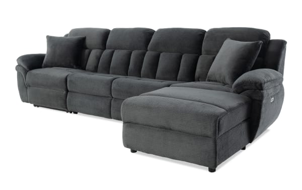 Dark gray sectional sofa with plush textured fabric upholstery, featuring a chaise lounge on the right side and two matching throw pillows.