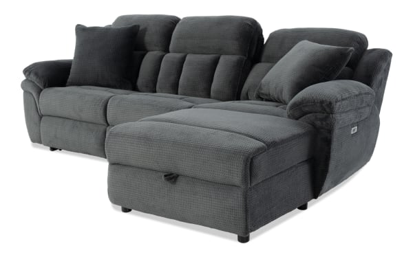 Dark gray fabric sectional sofa with plush cushioning, padded armrests, and two matching throw pillows, featuring a textured upholstery and a reclining chaise lounge.