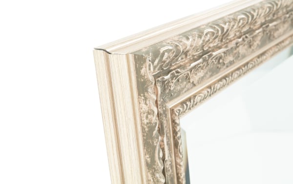 Close-up of a decorative vintage-style mirror corner with an ornate, distressed silver and beige wooden frame.