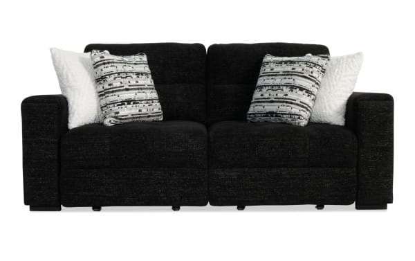 Black fabric reclining loveseat sofa with plush cushioning, featuring two patterned gray and black pillows and two white textured throw pillows.