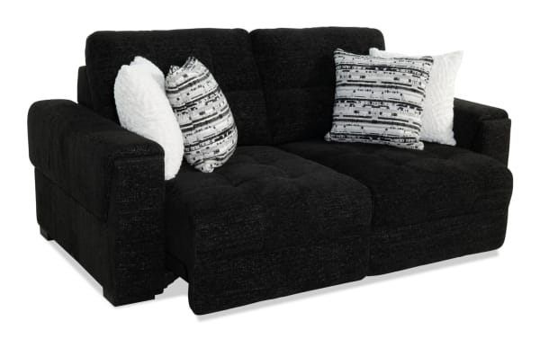 Black fabric reclining loveseat with plush cushioning, featuring two white and two black-and-white patterned throw pillows, ideal for modern living rooms.