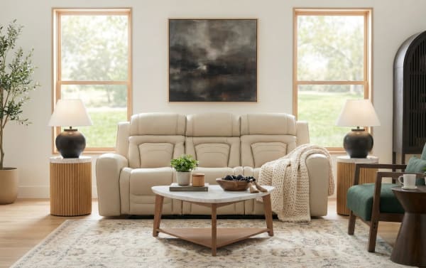 Modern living room with beige leather reclining sofa, wooden coffee table with marble top, neutral area rug, twin side tables with black ceramic lamps, and large abstract wall art.