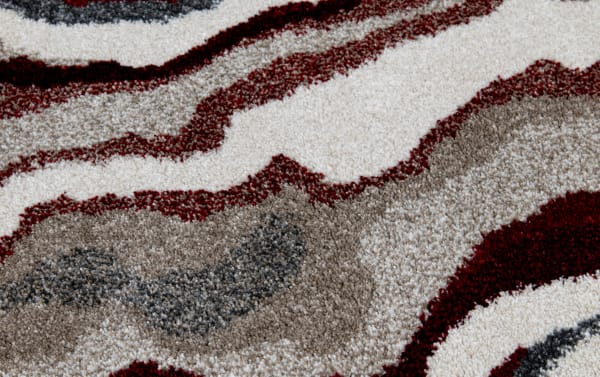 Close-up of a multicolored abstract patterned carpet with beige, brown, red, and gray tones, showcasing texture and design details.