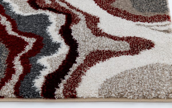 Close-up of a textured area rug with abstract wavy patterns in red, gray, beige, and white colors, showcasing thick plush material and modern design.