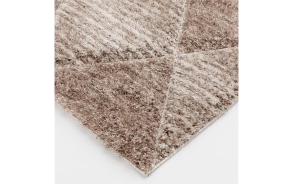 Corner view of a beige and light brown geometric patterned shaggy area rug with a soft, textured pile and subtle color variations.