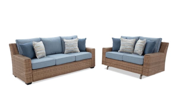 Outdoor patio furniture set with two wicker sofas featuring blue cushions and striped throw pillows, ideal for garden or porch seating.