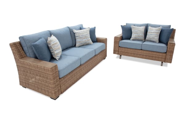 Outdoor wicker sofa set with blue cushions and striped accent pillows, featuring a three-seater and a two-seater with wooden armrests.