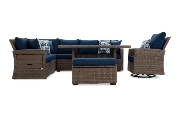 Outdoor patio furniture set featuring a brown wicker sectional sofa with navy blue cushions, matching swivel chair, ottoman, and rectangular coffee table.