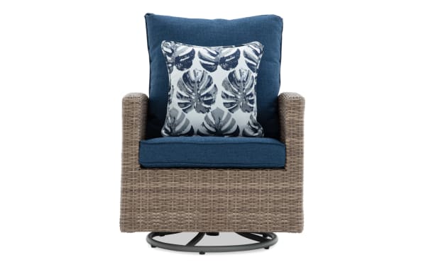 Outdoor swivel armchair with woven rattan frame, blue fabric cushions, and a decorative leaf-patterned throw pillow.