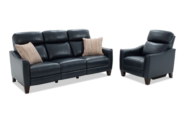 Black leather reclining sofa set with three seats and matching armchair, featuring cushioned headrests, wooden legs, and two patterned throw pillows.