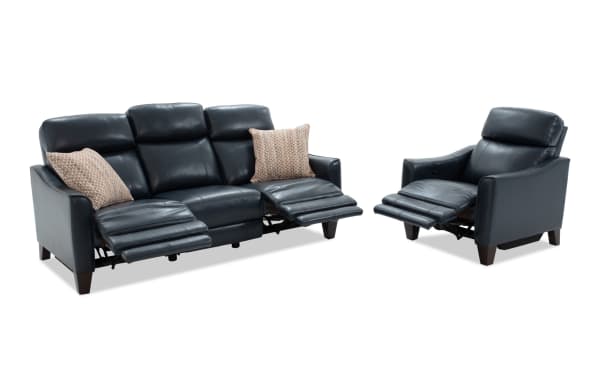 Black leather reclining sofa and armchair set with padded headrests, wooden legs, and patterned accent pillows, designed for living room comfort.