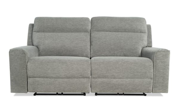 Modern gray fabric reclining loveseat with plush cushioning, wide armrests, and a contemporary design ideal for living room comfort.